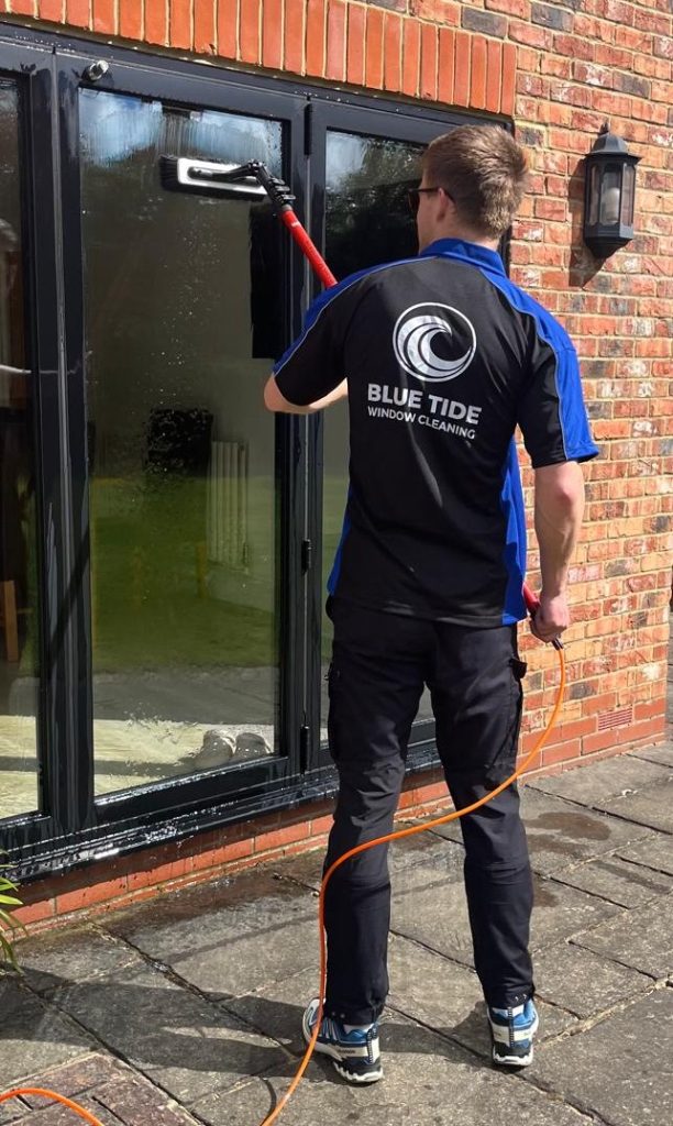Window cleaner from Blue Tide Window Cleaning using a water-fed pole to clean patio doors on a residential home in Kings Hill, Kent